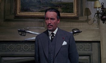 Movie still from “The Devil Rides Out” (1968), directed by Terence Fisher – A man in a suit and tie standing in front of a painting; Medium shot, Low angle