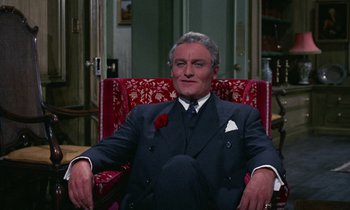 Movie still from “The Devil Rides Out” (1968), directed by Terence Fisher – An older man sitting in a chair with a rose in his mouth; Medium shot, High angle