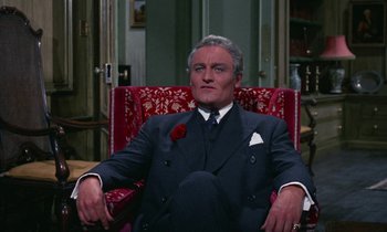 Movie still from “The Devil Rides Out” (1968), directed by Terence Fisher – An older man sitting in a chair with a rose in his mouth; Medium shot, High angle