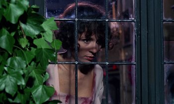 Movie still from “The Devil Rides Out” (1968), directed by Terence Fisher – A woman looking through a window at a plant; Close Up shot, Low angle