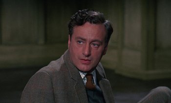 Movie still from “The Devil Rides Out” (1968), directed by Terence Fisher – A person wearing a suit and tie; Close Up shot, Over the shoulder angle
