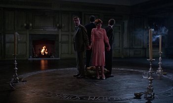Movie still from “The Devil Rides Out” (1968), directed by Terence Fisher – A group of people standing in front of a fire place; Wide shot, High angle
