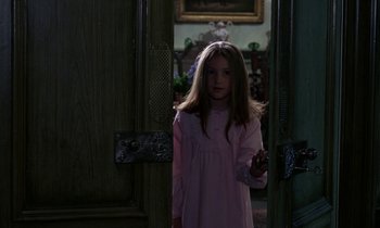 Movie still from “The Devil Rides Out” (1968), directed by Terence Fisher – A girl in a pink dress standing in front of an open door; Medium shot, Over the shoulder angle