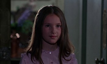 Movie still from “The Devil Rides Out” (1968), directed by Terence Fisher – A young girl in a pink shirt is posing for a picture; Close Up shot, Over the shoulder angle
