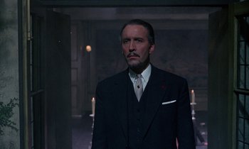 Movie still from “The Devil Rides Out” (1968), directed by Terence Fisher – A man in a suit and tie standing in a room; Medium shot, Low angle