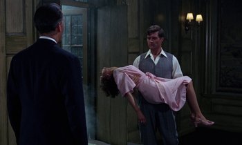 Movie still from “The Devil Rides Out” (1968), directed by Terence Fisher – A man and a woman are holding a dead body in a room; Wide shot, High angle
