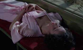 Movie still from “The Devil Rides Out” (1968), directed by Terence Fisher – A woman laying on the ground in a pink robe; Medium shot, High angle