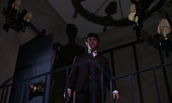 Movie still from “The Devil Rides Out” (1968), directed by Terence Fisher – A man wearing a suit and tie standing in a room; Medium shot, Low angle