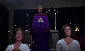 Movie still from “The Devil Rides Out” (1968), directed by Terence Fisher – A man in a purple robe standing in front of two women; Medium shot, Low angle