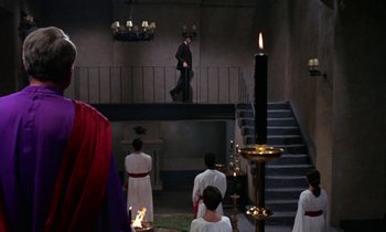 Movie still from “The Devil Rides Out” (1968), directed by Terence Fisher – A group of people standing in a room with candles; Wide shot, Over the shoulder angle