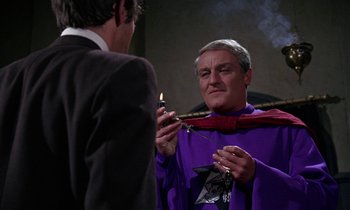 Movie still from “The Devil Rides Out” (1968), directed by Terence Fisher – A man in a purple robe holding a lit candle; Medium shot, Low angle