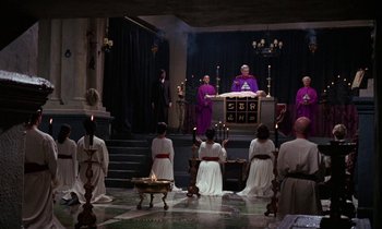Movie still from “The Devil Rides Out” (1968), directed by Terence Fisher – A group of people dressed in purple and white standing in front of an altar; Wide shot, High angle