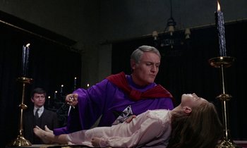 Movie still from “The Devil Rides Out” (1968), directed by Terence Fisher – A man in a purple robe and a girl in a pink robe; Medium shot, Over the shoulder angle