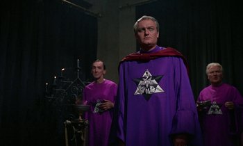 Movie still from “The Devil Rides Out” (1968), directed by Terence Fisher – Two men dressed in purple and one is holding a book; Medium shot, Low angle