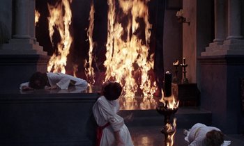 Movie still from “The Devil Rides Out” (1968), directed by Terence Fisher – A woman sitting in front of a fire; Wide shot, High angle