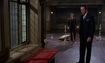 Movie still from “The Devil Rides Out” (1968), directed by Terence Fisher – Two men in suits and ties standing in front of a mirror; Wide shot, High angle