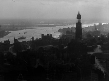 Movie still from “The Devil Strikes at Night” (1957), directed by Robert Siodmak – A black and white photo of a city with a river in the background; Extreme Wide shot, High angle