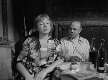Movie still from “The Devil Strikes at Night” (1957), directed by Robert Siodmak – An older man and a woman sitting at a table; Medium shot, Over the shoulder angle