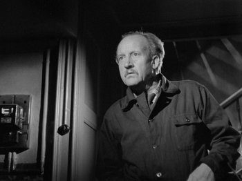 Movie still from “The Devil Strikes at Night” (1957), directed by Robert Siodmak – An older man standing in front of a window; Medium shot, Low angle