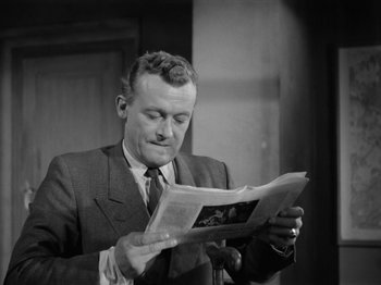 Movie still from “The Devil Strikes at Night” (1957), directed by Robert Siodmak – A black and white photo of a man reading a newspaper; Close Up shot, Low angle