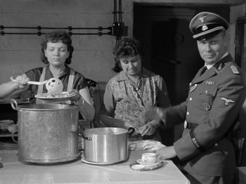 Movie still from “The Devil Strikes at Night” (1957), directed by Robert Siodmak – A black - and - white photo of a man and two women preparing a meal; Medium shot, High angle