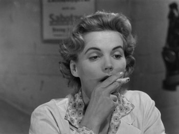 Movie still from “The Devil Strikes at Night” (1957), directed by Robert Siodmak – A black - and - white photo of a woman smoking a cigarette; Close Up shot, Low angle
