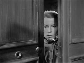 Movie still from “The Devil Strikes at Night” (1957), directed by Robert Siodmak – A black - and - white photo of a woman looking through a door; Close Up shot, Over the shoulder angle