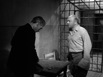 Movie still from “The Devil Strikes at Night” (1957), directed by Robert Siodmak – Two men standing next to each other at a table; Medium shot, Over the shoulder angle