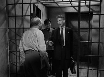 Movie still from “The Devil Strikes at Night” (1957), directed by Robert Siodmak – A group of men standing next to each other in a jail cell; Medium shot, High angle