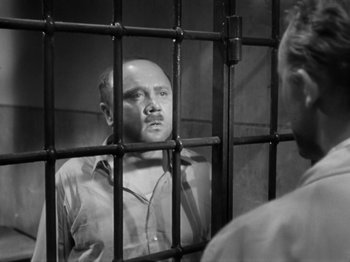 Movie still from “The Devil Strikes at Night” (1957), directed by Robert Siodmak – A man standing behind bars in a jail cell; Close Up shot, Over the shoulder angle