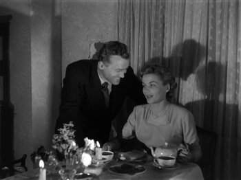 Movie still from “The Devil Strikes at Night” (1957), directed by Robert Siodmak – An old photo of a man and a woman sitting at a dinner table; Medium shot, High angle