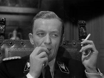 Movie still from “The Devil Strikes at Night” (1957), directed by Robert Siodmak – A man smoking a cigarette while holding a cell phone; Close Up shot, Low angle