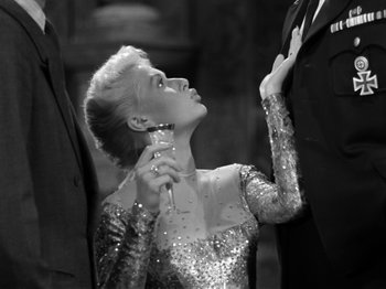 Movie still from “The Devil Strikes at Night” (1957), directed by Robert Siodmak – A black and white photo of a woman holding a wine glass; Medium shot, Low angle