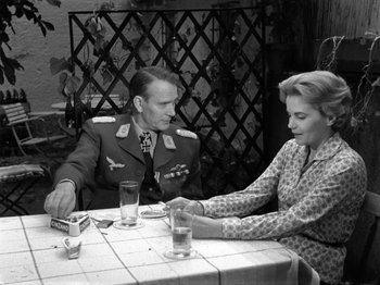 Movie still from “The Devil Strikes at Night” (1957), directed by Robert Siodmak – An older man and woman sitting at a table; Medium shot, Over the shoulder angle