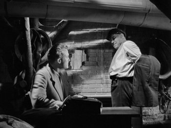 Movie still from “The Devil Strikes at Night” (1957), directed by Robert Siodmak – Two men are talking to each other in an industrial setting; Medium shot, Low angle