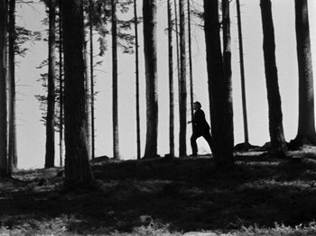 Movie still from “The Devil Strikes at Night” (1957), directed by Robert Siodmak – A person standing in the middle of a forest; Extreme Wide shot, Low angle