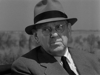 Movie still from “The Devil Strikes at Night” (1957), directed by Robert Siodmak – An older man wearing a hat and glasses; Close Up shot, Over the shoulder angle