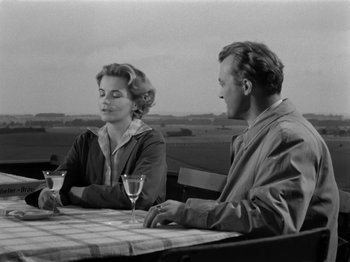 Movie still from “The Devil Strikes at Night” (1957), directed by Robert Siodmak – A man and a woman sitting at a table with wine glasses; Medium shot, Over the shoulder angle