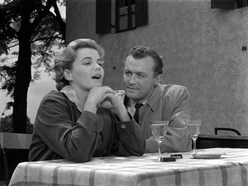 Movie still from “The Devil Strikes at Night” (1957), directed by Robert Siodmak – An old photo of a man and a woman sitting at a table; Medium shot, Over the shoulder angle