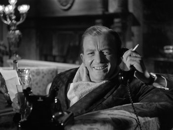 Movie still from “The Devil Strikes at Night” (1957), directed by Robert Siodmak – A black and white photo of a man talking on a phone; Medium shot, High angle