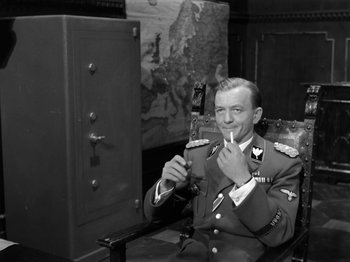 Movie still from “The Devil Strikes at Night” (1957), directed by Robert Siodmak – A man in uniform sitting in a chair smoking a cigarette; Medium shot, High angle