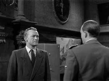Movie still from “The Devil Strikes at Night” (1957), directed by Robert Siodmak – A man in a suit and tie standing next to another man; Medium shot, Over the shoulder angle