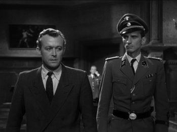 Movie still from “The Devil Strikes at Night” (1957), directed by Robert Siodmak – A man and a man in a suit standing next to each other; Medium shot, Over the shoulder angle