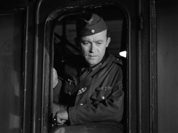 Movie still from “The Devil Strikes at Night” (1957), directed by Robert Siodmak – A man in a military uniform sitting inside a train; Medium shot, Low angle