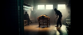 Movie still from “The Devil's Double” (2011), directed by Lee Tamahori – A man is lying on a table in a room with three people; Wide shot, High angle