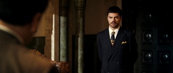 Movie still from “The Devil's Double” (2011), directed by Lee Tamahori – A man wearing a suit and tie standing in a room; Medium shot, Low angle