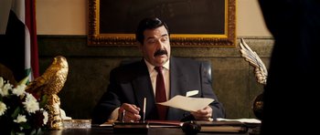 Movie still from “The Devil's Double” (2011), directed by Lee Tamahori – A man sitting at a desk in front of a piece of paper; Medium shot, Over the shoulder angle