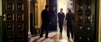 Movie still from “The Devil's Double” (2011), directed by Lee Tamahori – A group of men in suits standing in front of a doorway; Wide shot, Over the shoulder angle