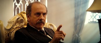 Movie still from “The Devil's Double” (2011), directed by Lee Tamahori – An older man in a suit and tie pointing to the side; Close Up shot, Low angle