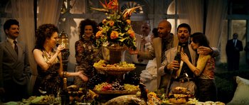 Movie still from “The Devil's Double” (2011), directed by Lee Tamahori – A group of people standing around a table with food on top of it; Wide shot, High angle